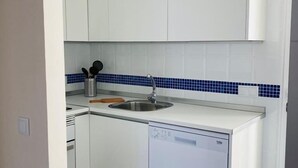 Una cocina compacta con armarios blancos, un salpicadero de azulejos azules, un lavamanos de acero inoxidable y un lavavajillas.