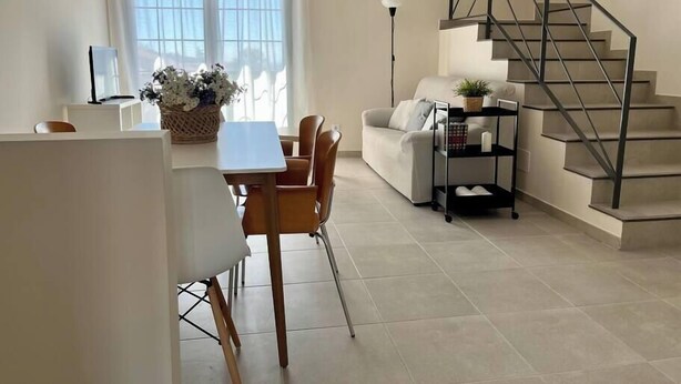 Una sala de estar moderna con comedor, una escalera y un ventanal con cortinas ligeras.