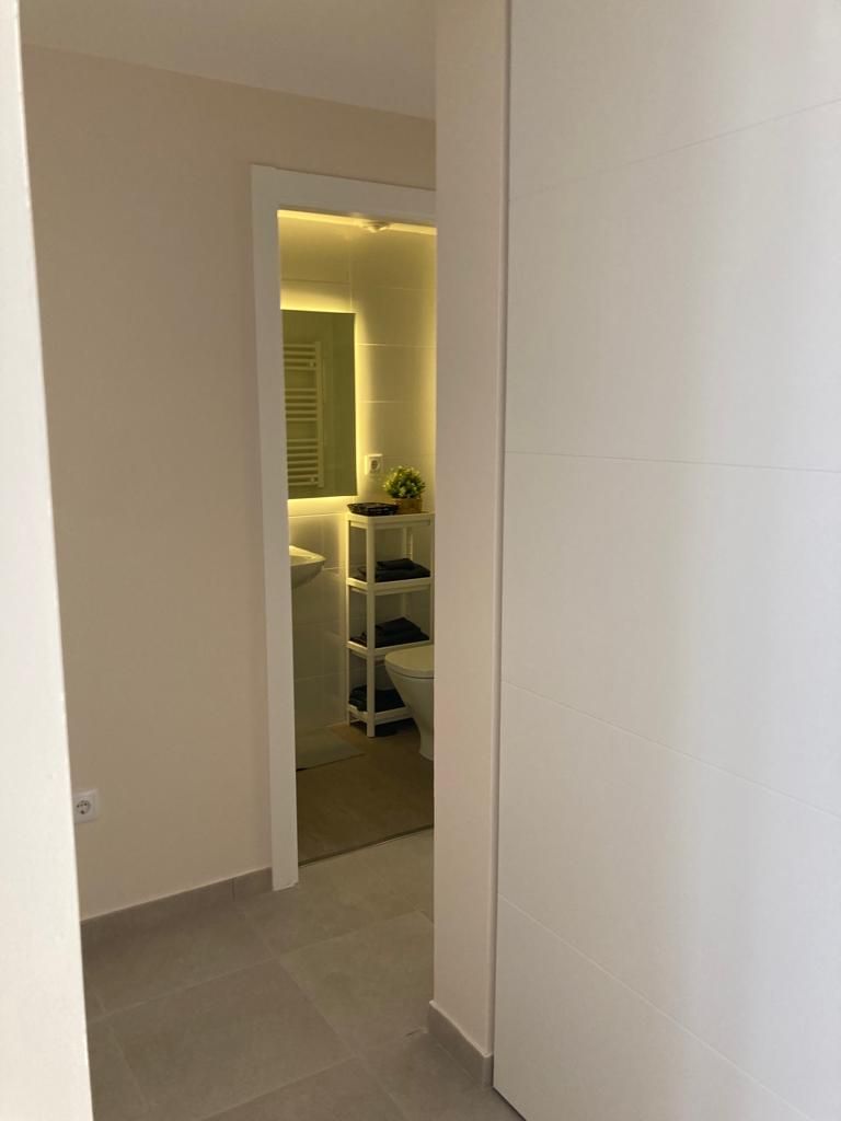 Un pasillo estrecho que conduce a un baño con inodoro, estantes y un espejo.