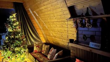 A cozy room with a wooden ceiling, a Christmas tree, a sofa, and a fireplace.