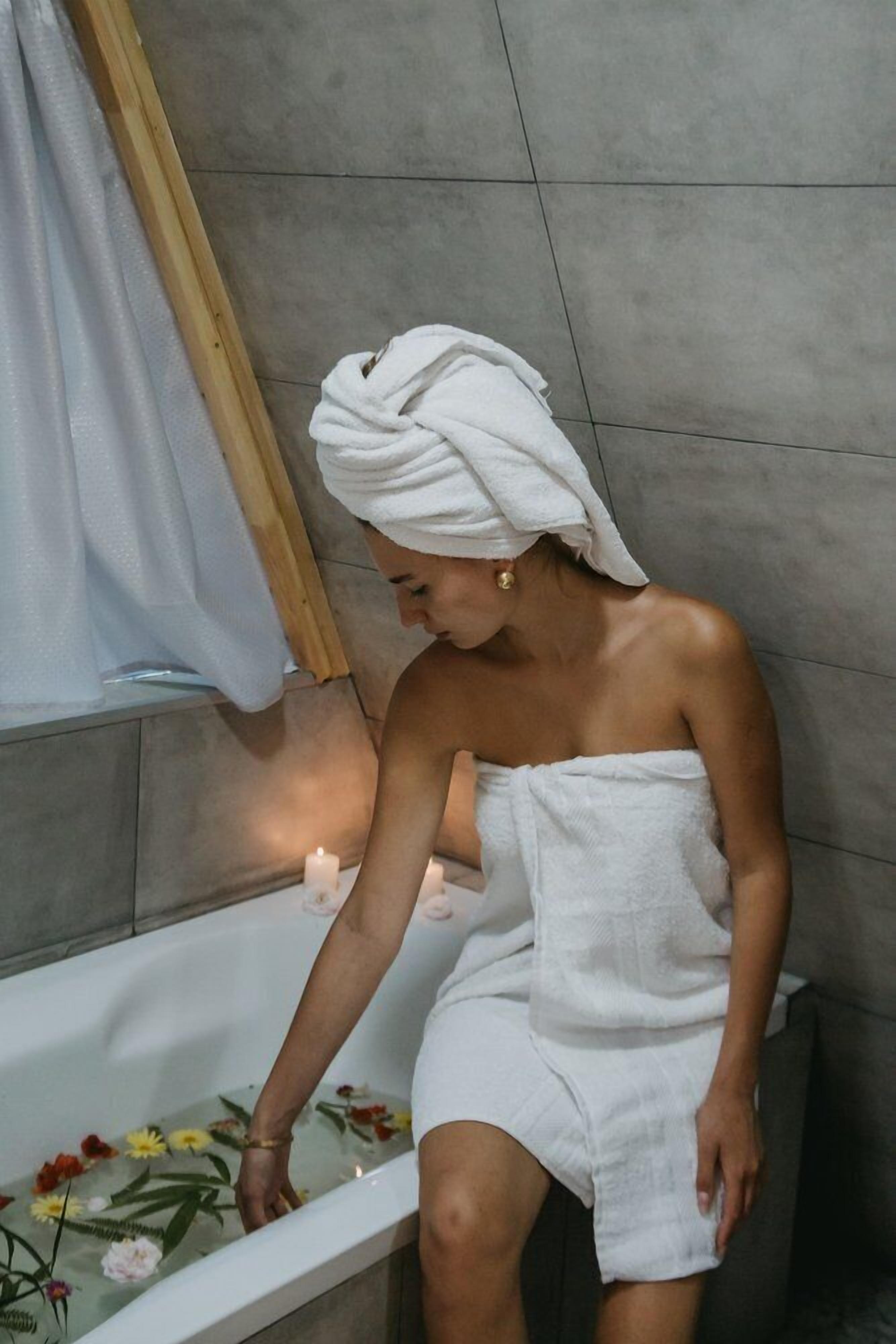 A person sitting in a bathtub with floral arrangements.