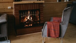 A cozy room with a brick fireplace, wooden shelves with decorative items, and a comfortable chair. - Thomas Hut (Khelvachauri)