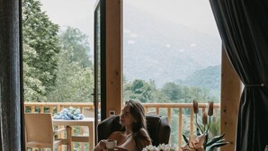 A cozy room with a wooden floor, a sofa, a table with a vase of flowers, and a view of a balcony with chairs and a table outside. - Thomas Hut (Khelvachauri)