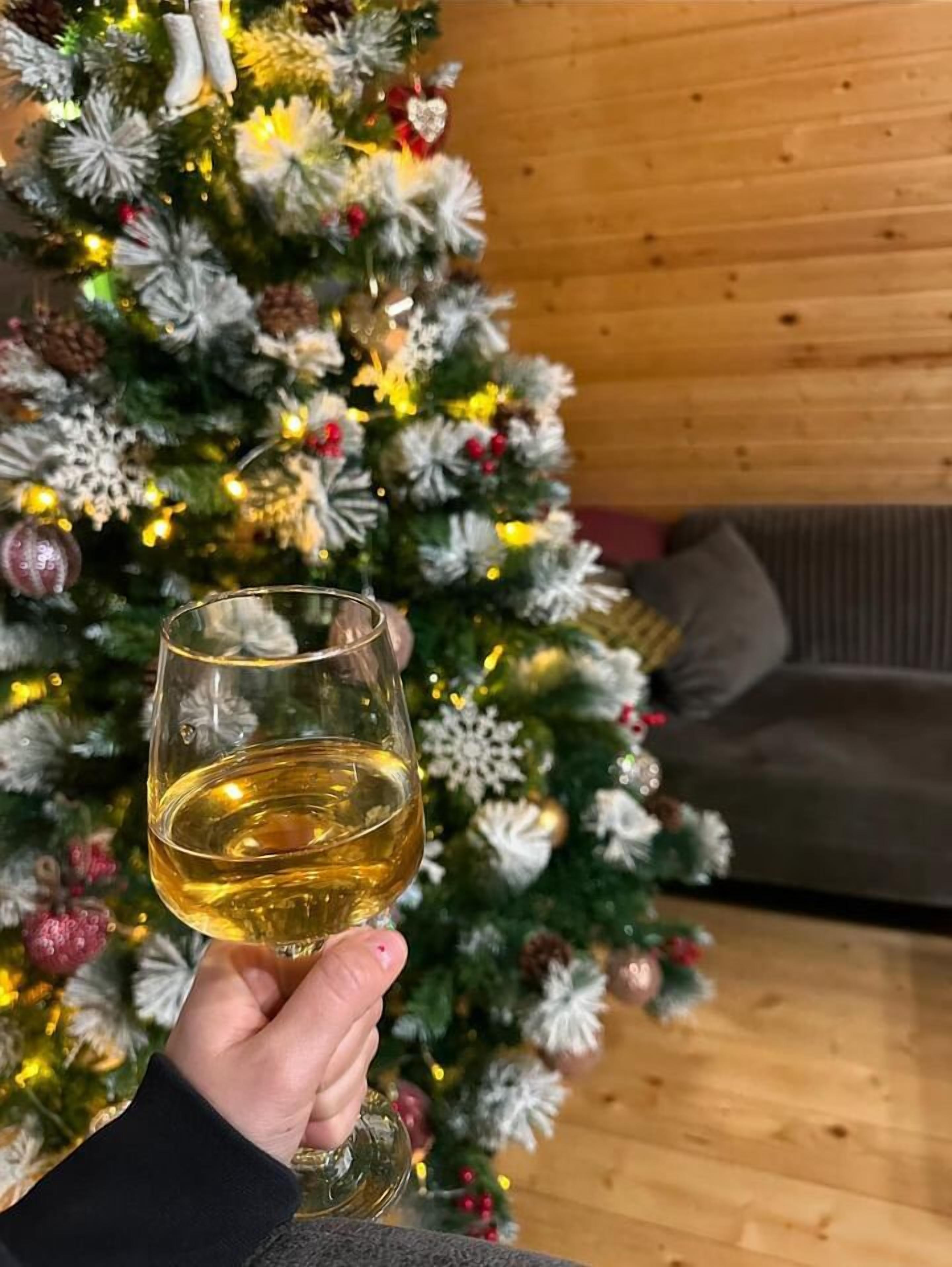 A hand holding a glass of white wine in front of a decorated Christmas tree.