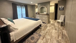 A bedroom with a large bed, a dresser, a chair, and a mirror. - Modern 2-bdrm/2-bath mobile home, near Wildcat ATV Park, riders welcome! Wi-Fi! (Livingston)
