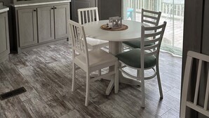 A dining area with a white table and chairs, a kitchen with light wood cabinets, and a view of a balcony with a railing. - Modern 2-bdrm/2-bath mobile home, near Wildcat ATV Park, riders welcome! Wi-Fi! (Livingston)