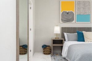 Un dormitorio con cama, mesita de noche, lámpara y una obra de arte en la pared.