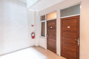 Un pasillo con dos puertas de madera, un extintor y suelo de baldosas.