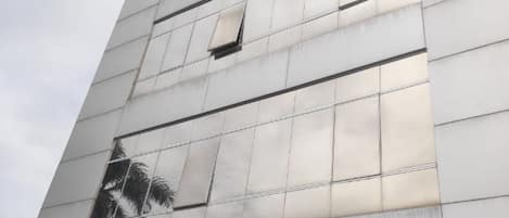 Fachada de edificio con superficie de vidrio reflectante y una ventana que refleja una palmera.