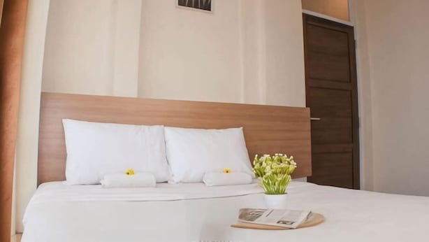 Ein ordentlich bezogenes Bett mit weißen Leinen und Kissen, ein kleiner Blumenstrauß in einer Vase und ein gerahmtes Bild an der Wand.