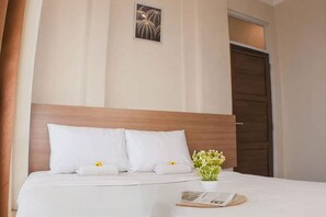 A neatly made bed with white linens and pillows, a small vase with flowers, and a framed picture on the wall. - The Kartini 8 Residence - Mangga Besar (Central Jakarta)
