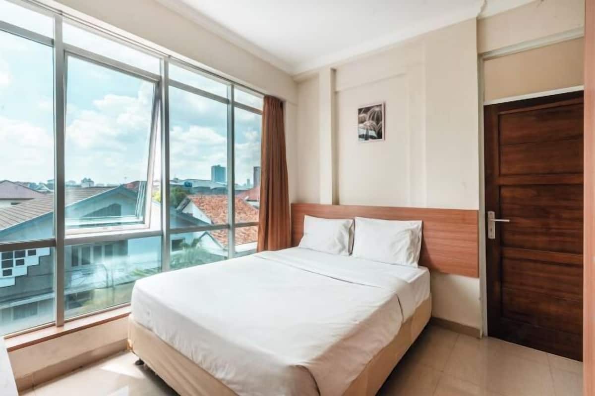 Habitación de hotel con un ventanal grande, una cama, una puerta de madera y un cuadro en la pared.