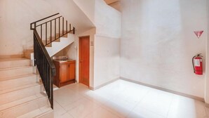 Eine Treppe mit schwarzer Geländer führt zu einer Zwischenebene. Ein Feuerlöscher ist an der rechten Wand angebracht.