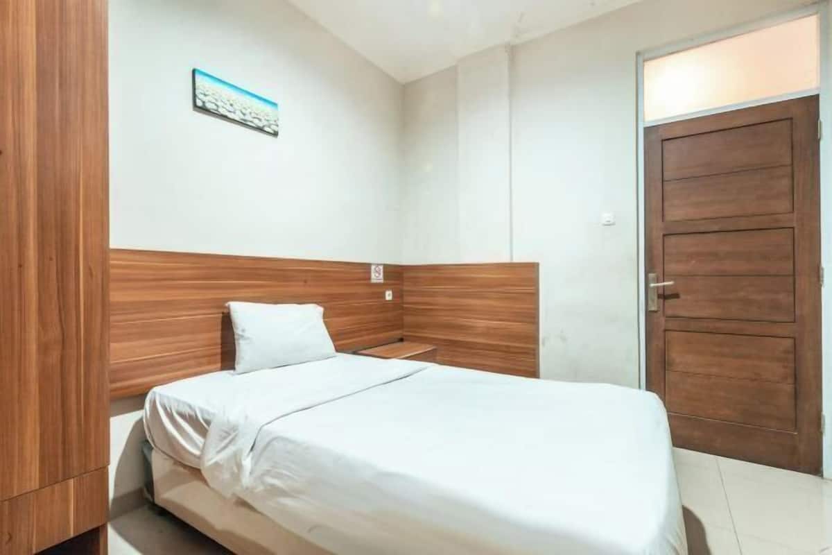 Un dormitorio con cabecera de madera, una cama individual, pared blanca y una puerta.