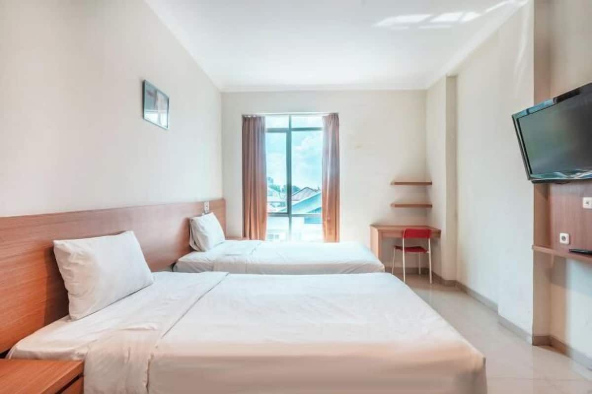 Habitación de hotel con dos camas, televisión, ventana con cortinas y vistas a edificios.