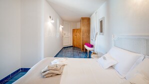 A hotel room with a bed, a bench, a wooden wardrobe, and a small table.