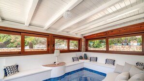 A sunlit room with a pool, wooden beams, and large windows overlooking a garden.