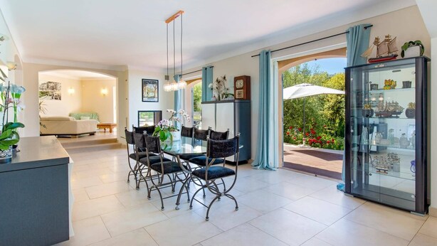 A spacious dining area with a glass table and chairs, a kitchen area with a refrigerator, and a glass cabinet with decorative items.