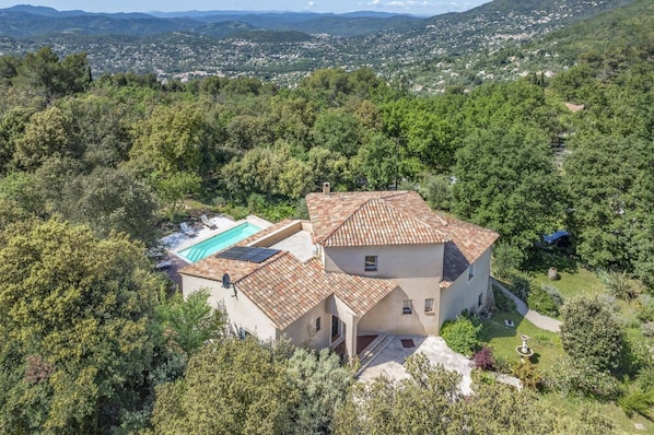 Una villa con piscina, rodeada de exuberante vegetación y colinas.