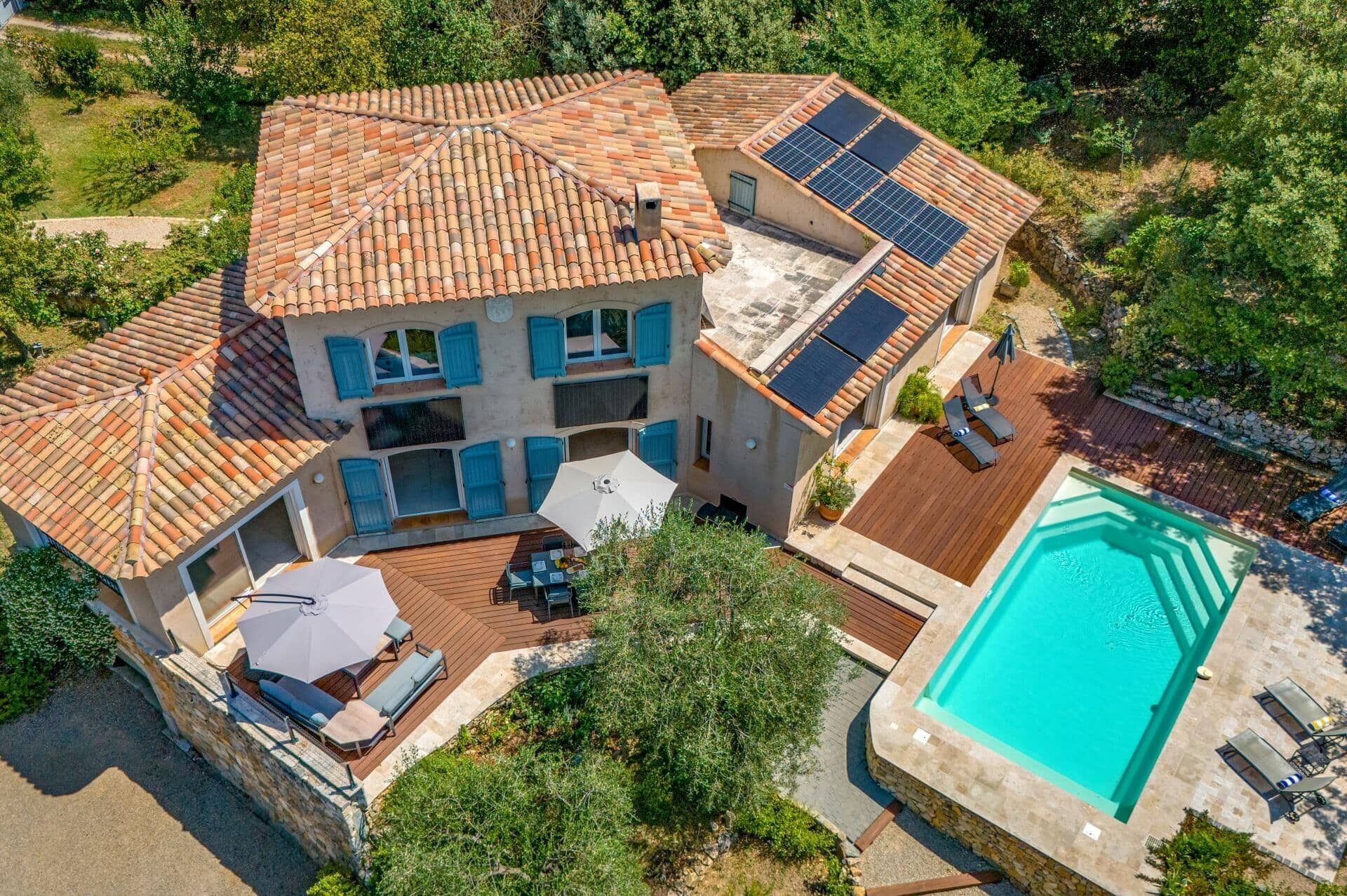 Una casa de dos pisos con piscina, paneles solares y un patio con mobiliario exterior.