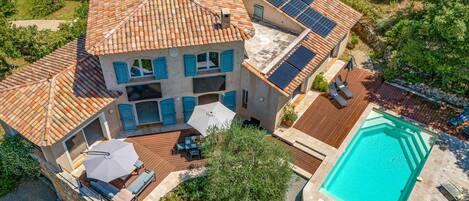 Una casa de dos pisos con piscina, paneles solares y un patio con mobiliario exterior.