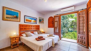 A double room with two beds, a wooden headboard, a nightstand, a small table, and a balcony with a view of greenery. - Villa Jacqueline by Villa Plus (Montgo de Toscamar)