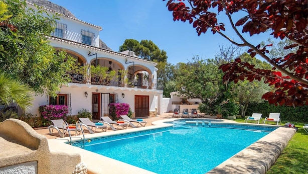 A swimming pool with lounge chairs, a white building with arches, and surrounding greenery. - Villa Jacqueline by Villa Plus (Montgo de Toscamar)