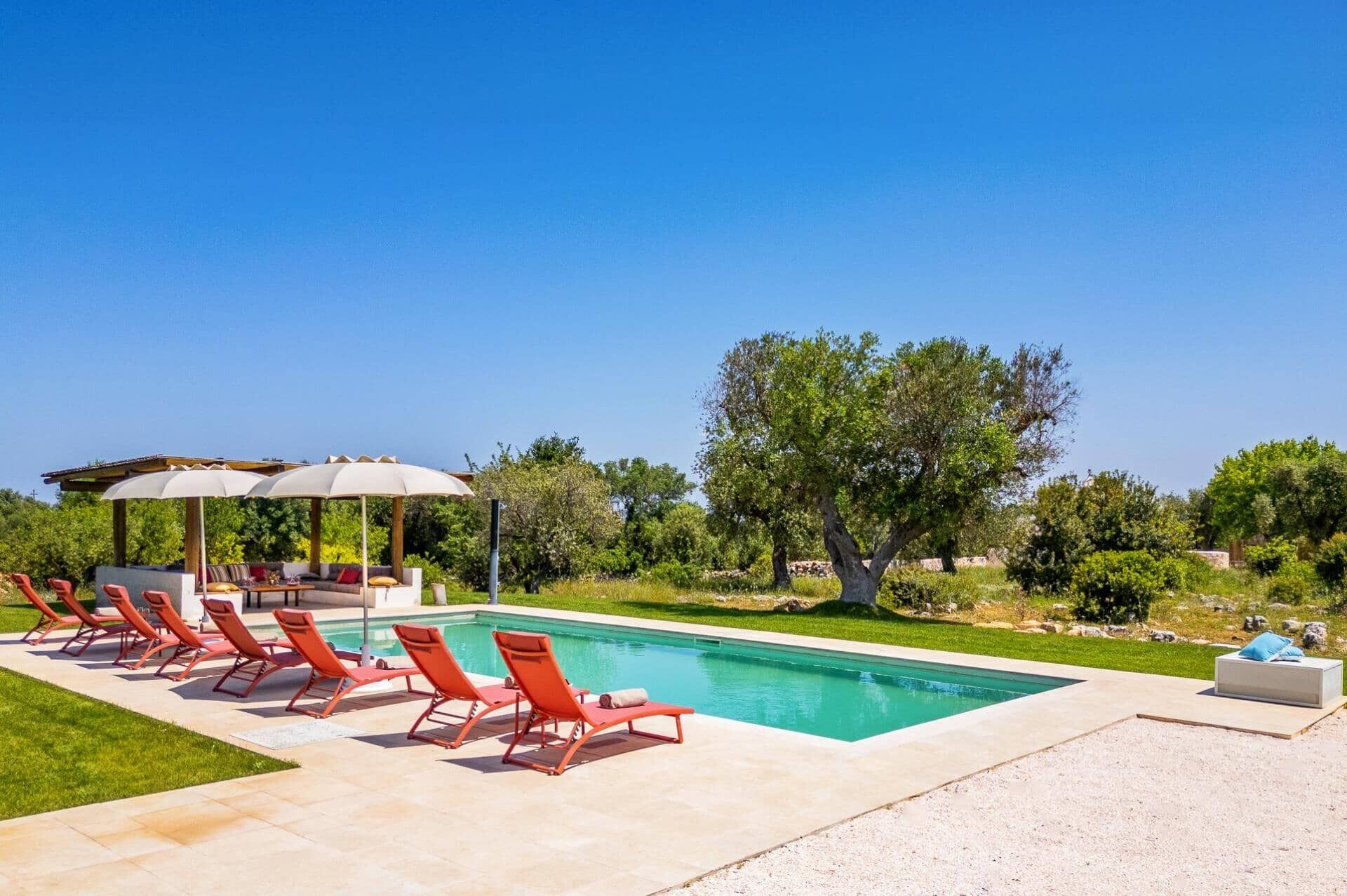 Ein Pool mit roten Liegestühlen und einem überdachten Sitzbereich.