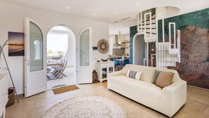 Un salón amplio con un sofá blanco grande, una zona de comedor con mesa y sillas, y una cocina con electrodomésticos modernos.
