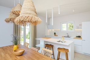 Une cuisine moderne avec des meubles blancs, un îlot central, des tabourets de bar et des luminaires suspendus en fibres tressées.