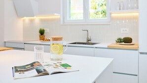 A kitchen with white cabinets, a window, a pitcher with lemon slices, a glass of water, and a magazine on the counter. - Hedera Estate, Villa Hedera XVIII (Mlini)
