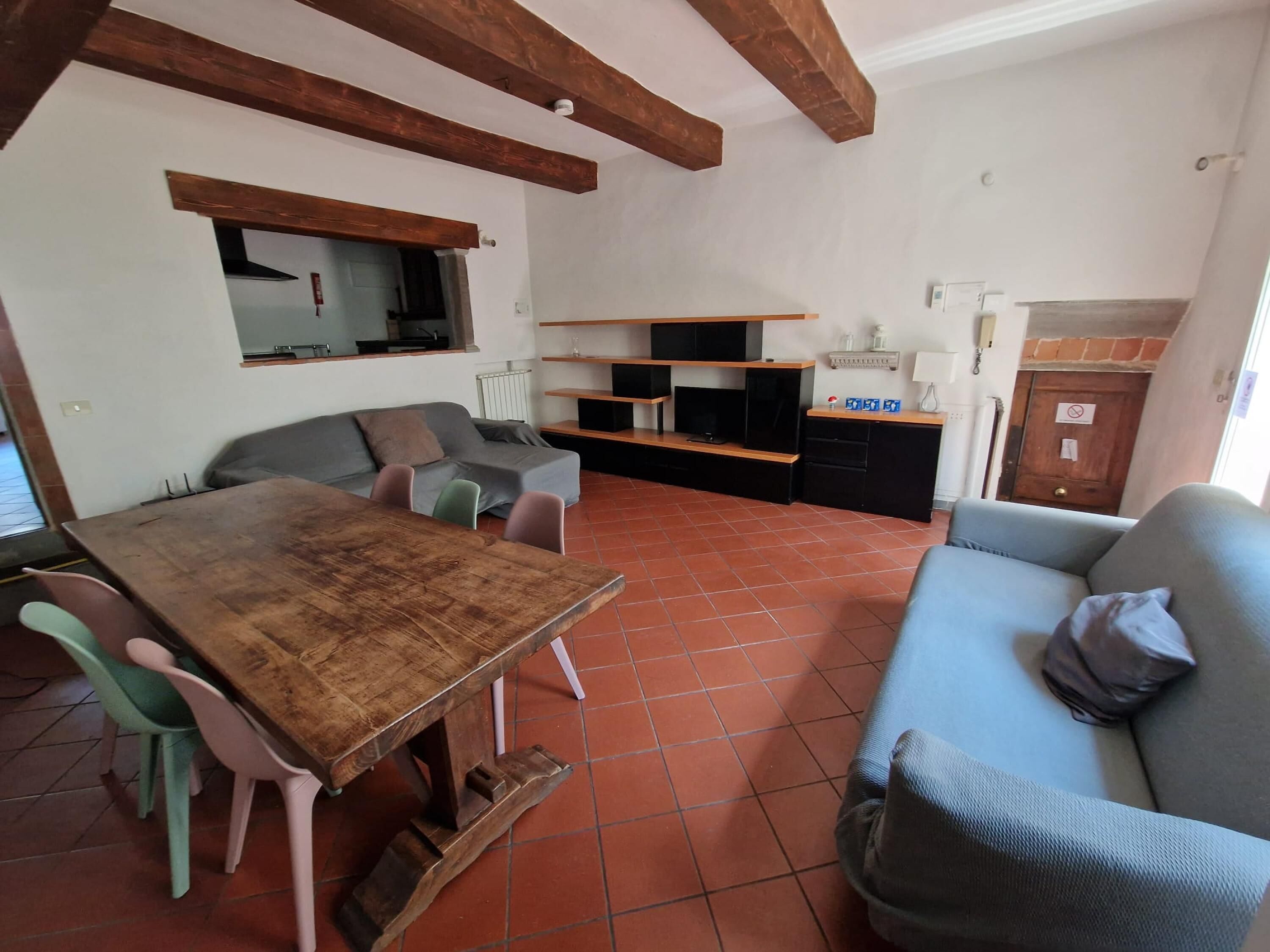 Un espace de vie compact comprenant une table à manger, des chaises, un canapé et un coin cuisine avec des étagères et un téléviseur.