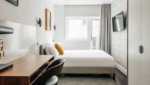 A modern hotel room with a bed, a desk, a chair, a TV, and a window with curtains.