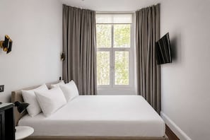 Une chambre d’hôtel équipée d’un lit, d’un bureau, d’une chaise, d’une télévision et d’une fenêtre avec des rideaux.