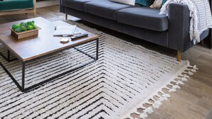 Un salon moderne avec un canapé gris, une table basse et une grande fenêtre ornée de rideaux blancs.