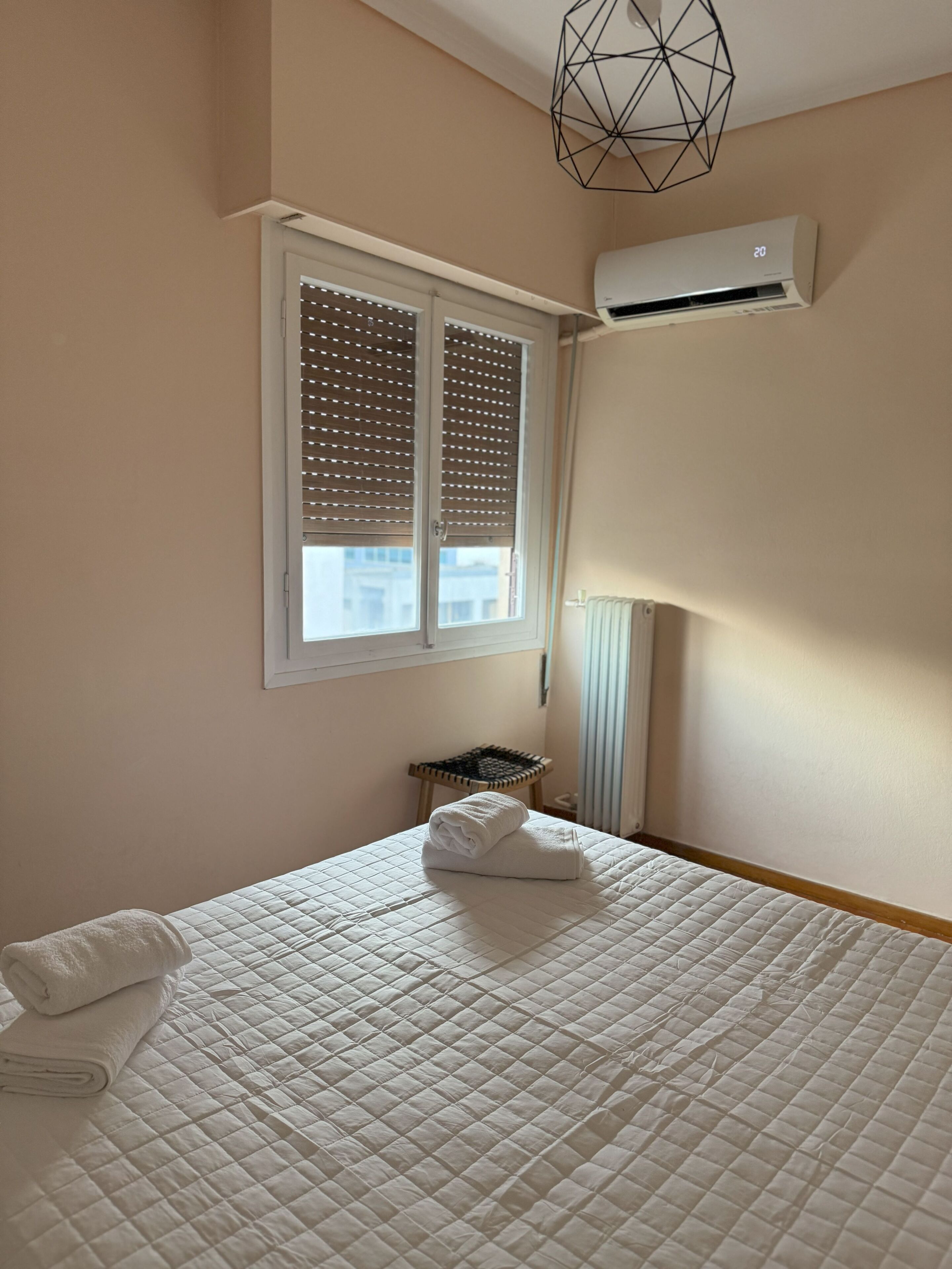 A bedroom with a bed, a window with blinds, an air conditioner, and a radiator.
