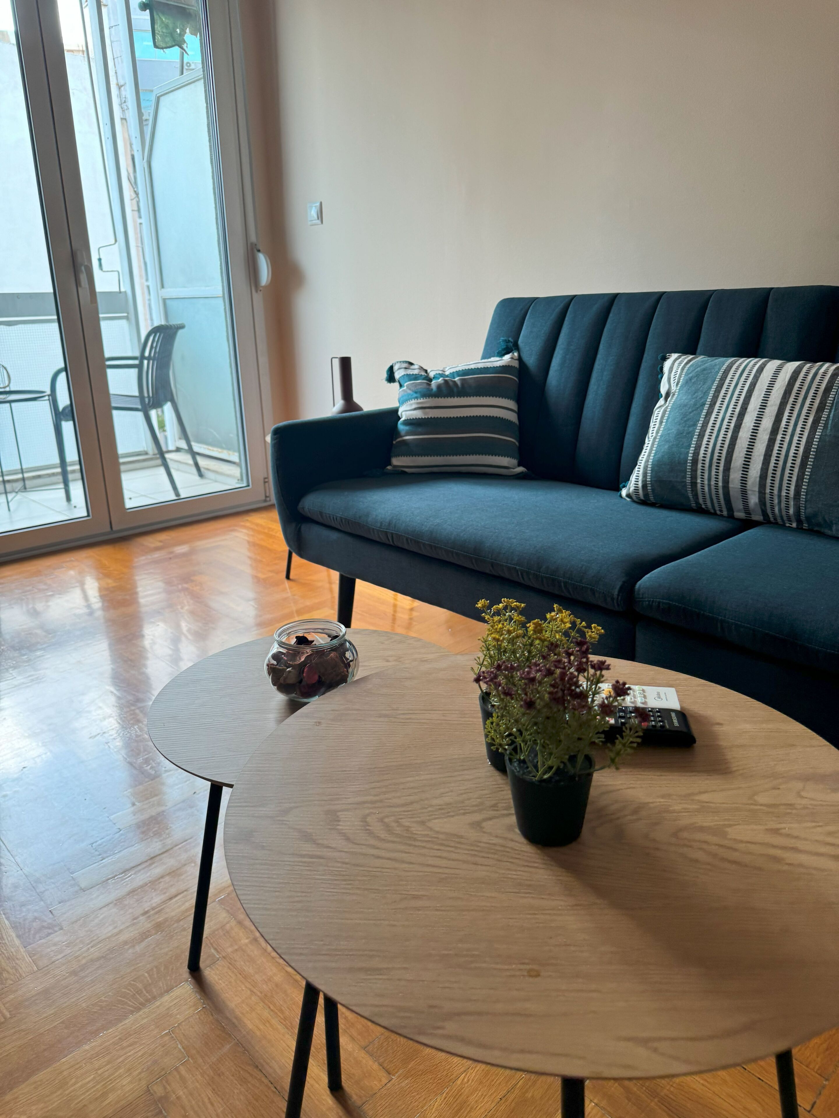 A living room with a dark blue sofa, a round wooden coffee table with a plant, and a glass table with decorative items.