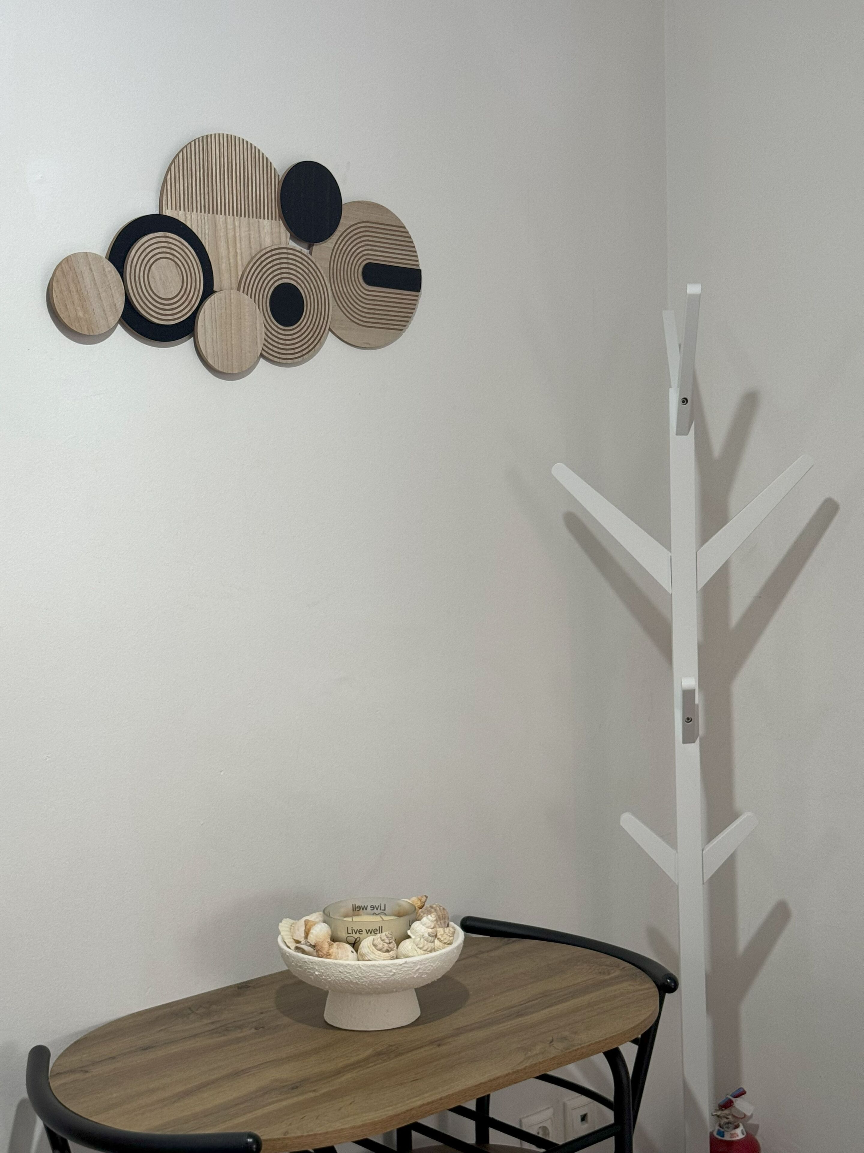 Un comedor con una mesa redonda de madera, un cuenco blanco con frutos secos y una obra de arte de madera colgada en la pared.
