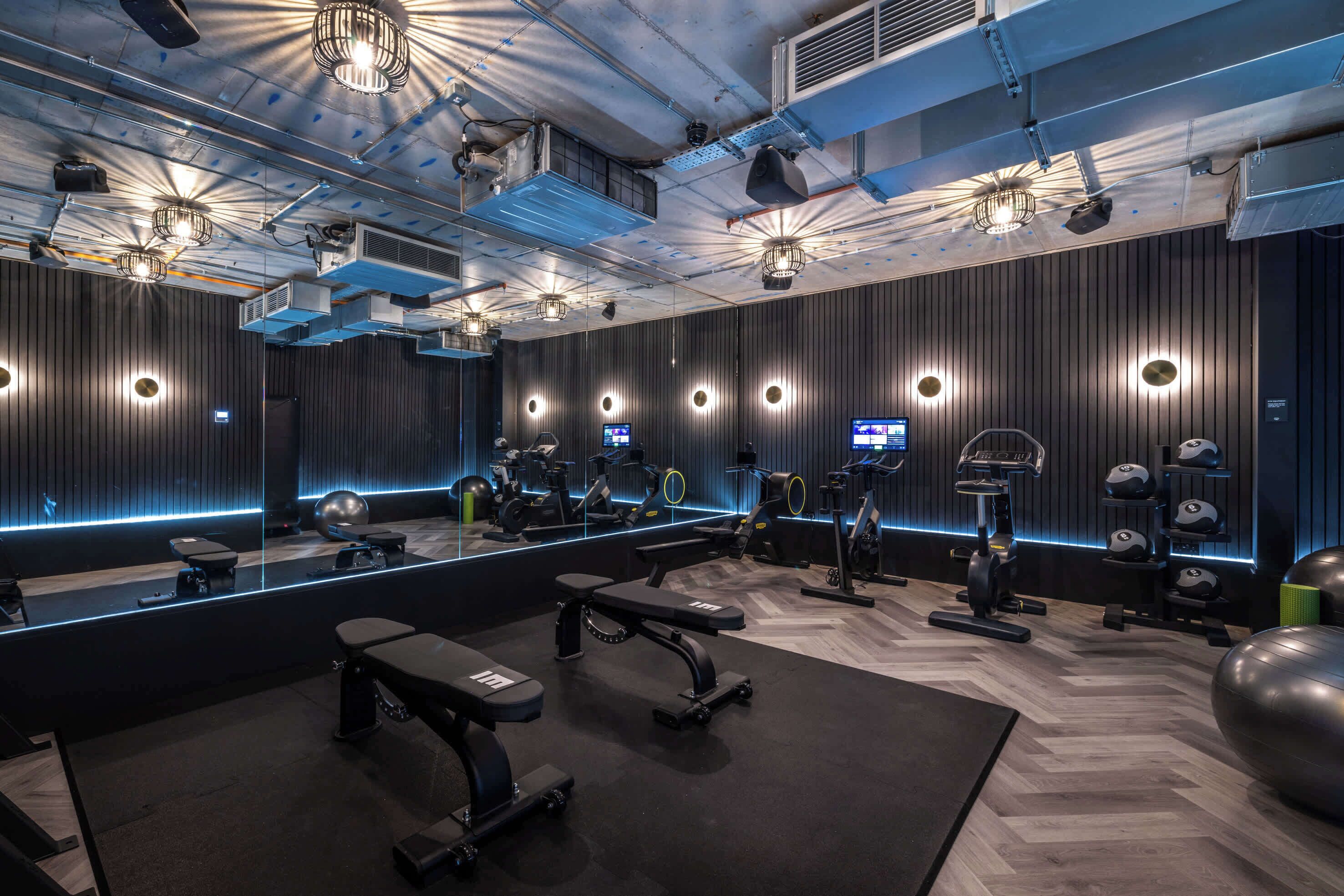 A modern gym with mirrored walls, various exercise equipment, and a central bench.
