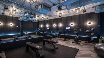 A modern gym with mirrored walls, various exercise equipment, and a central bench.