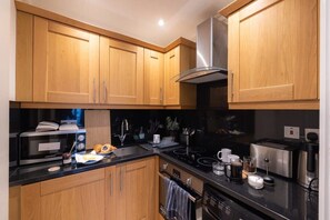 A modern kitchen with wooden cabinets, a stainless steel range hood, and various appliances including a microwave, toaster, and coffee maker.