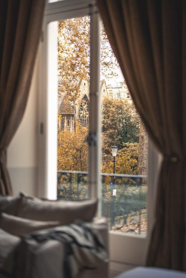 A room with a large window, curtains, and a view of a building with trees.