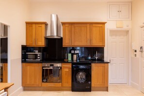 A compact kitchen with wooden cabinets, a microwave, a toaster, a coffee maker, and a washing machine.