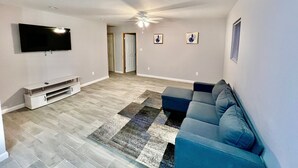 Una sala de estar con televisor de pantalla plana, ventilador de techo, sofá modular y alfombra estampada.