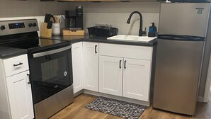 A modern kitchen with white cabinets, stainless steel appliances, a wooden floor, and a black and white patterned rug. - Cheerful cabin with KING bed and WiFi, AC in charming Plainview (Plainview)