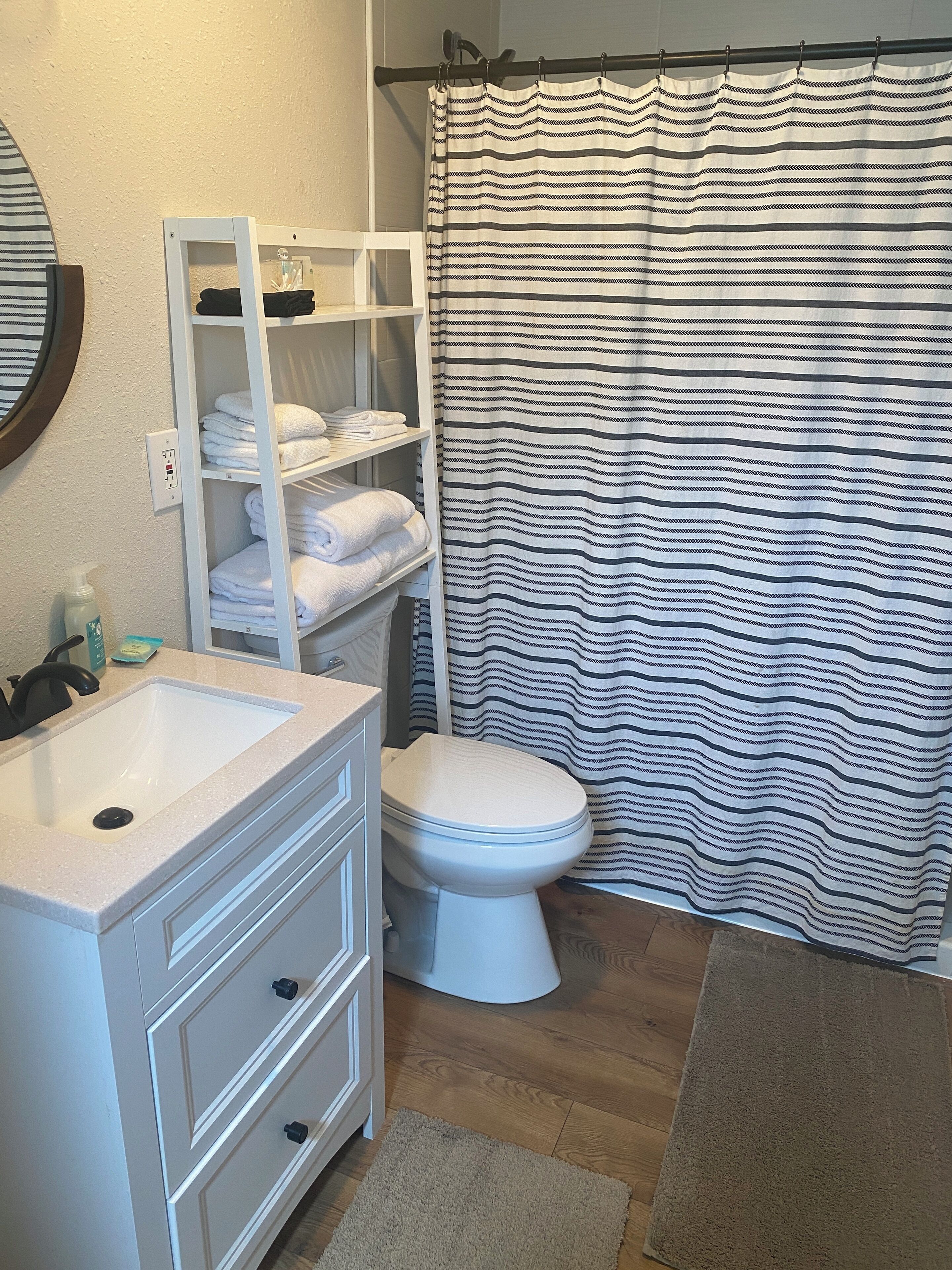 A bathroom with a white sink, a toilet, a towel rack with folded towels, and a striped shower curtain.