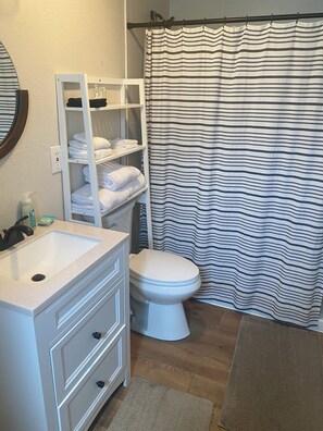 A bathroom with a white sink, a toilet, a towel rack with folded towels, and a striped shower curtain. - Cheerful cabin with KING bed and WiFi, AC in charming Plainview (Plainview)