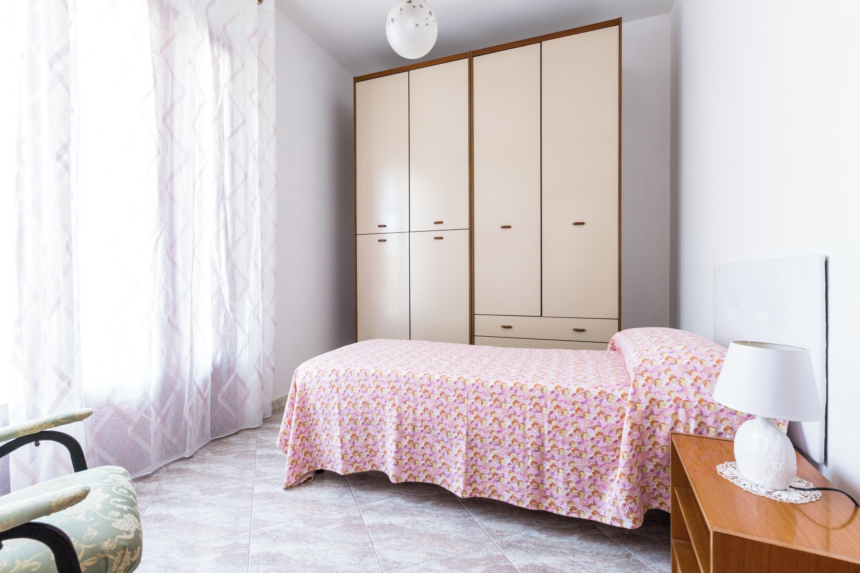 A bedroom with a bed, a wardrobe, a nightstand, and a lamp.