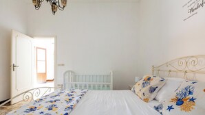 A bedroom with a white bed, floral bedding, a white crib, and a wall with a quote. - Cascina Mimì by BarbarHouse (Nardò)