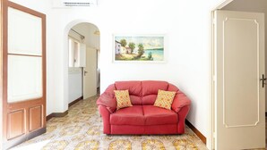 A red sofa with patterned cushions in a hallway with patterned flooring, a white door, and a framed landscape painting on the wall. - Cascina Mimì by BarbarHouse (Nardò)